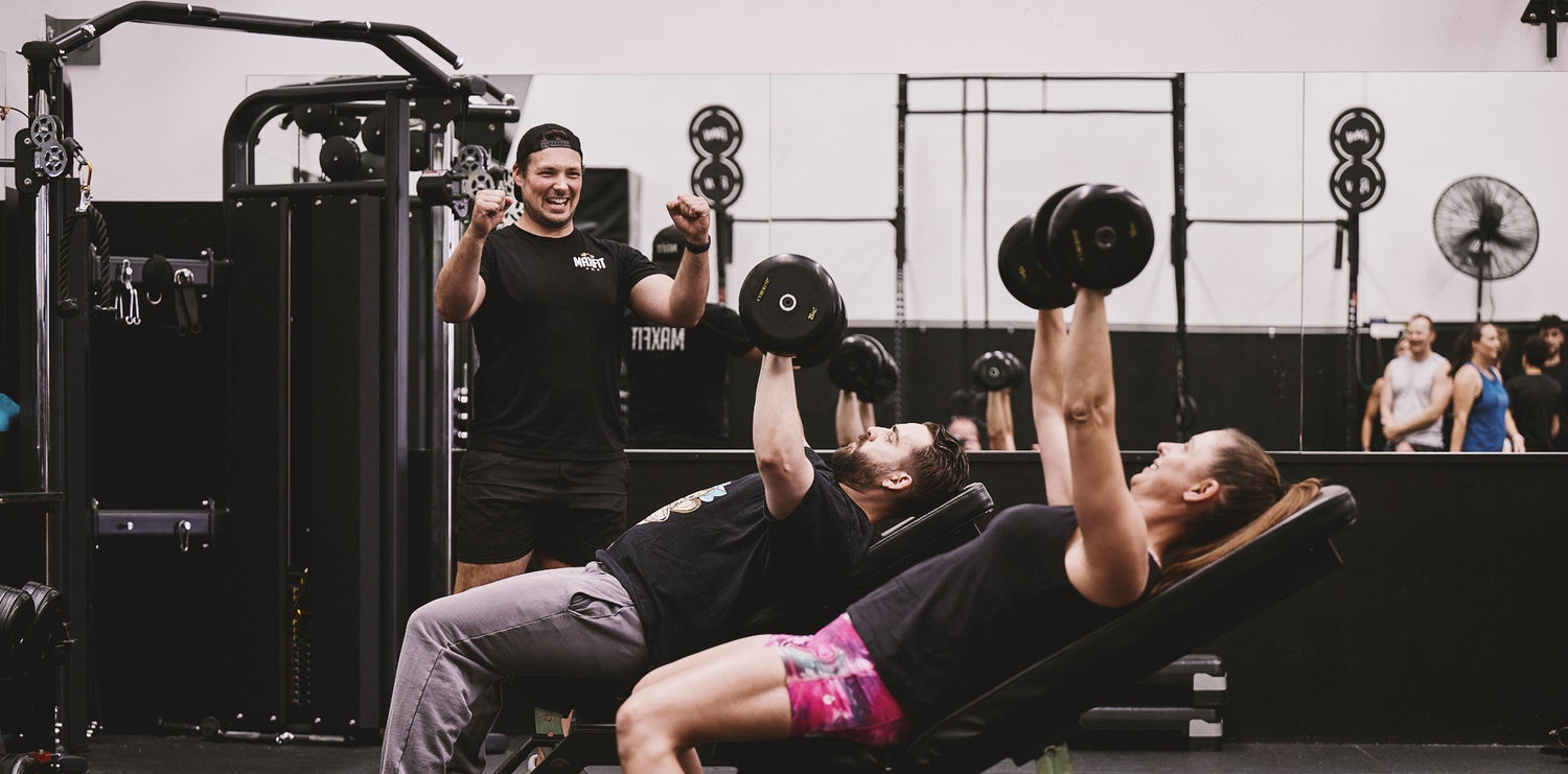 Person performing bench press with spotter in a gym setting