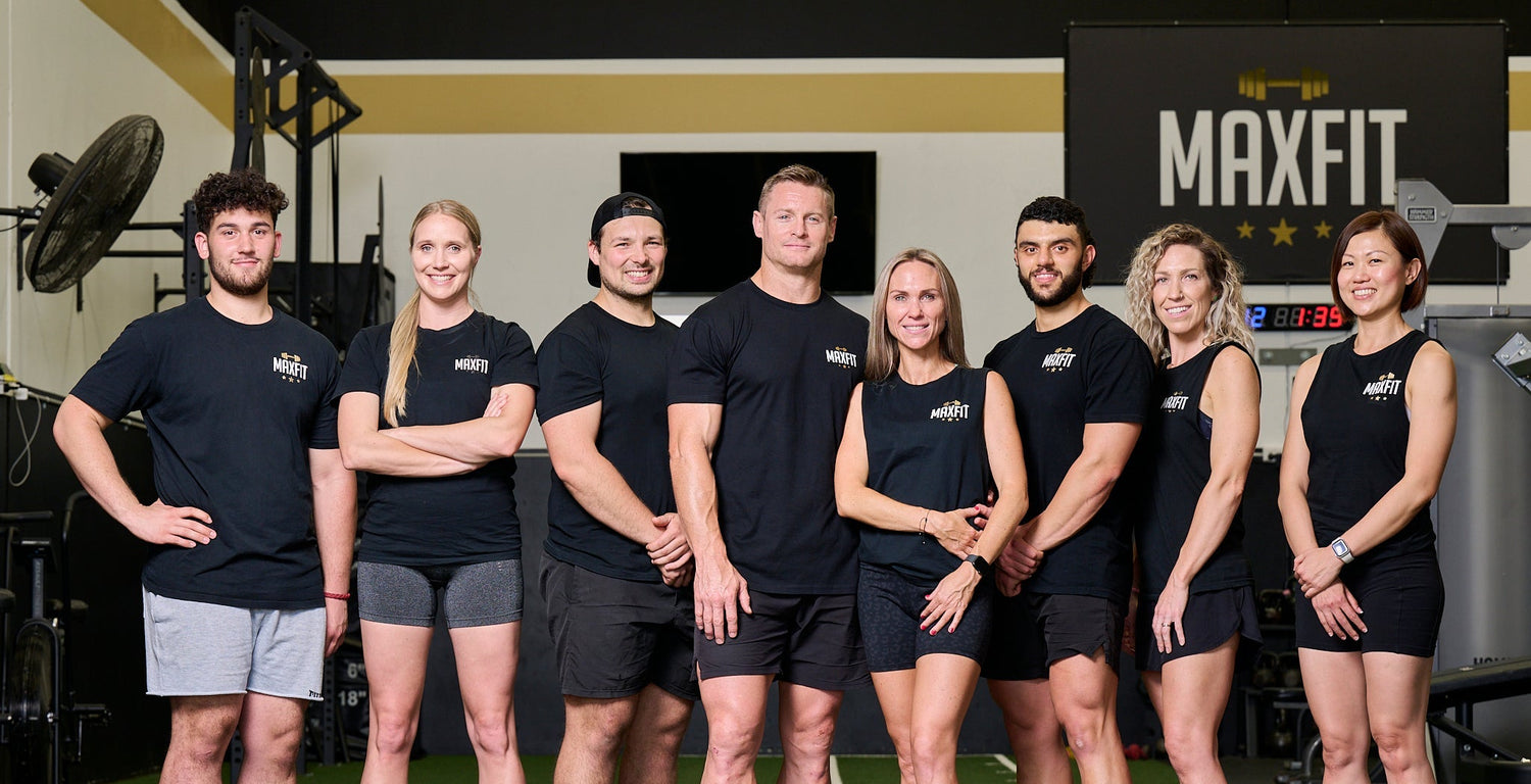 Group of people in fitness attire standing in a line with 'MAXFIT' branding in the background.